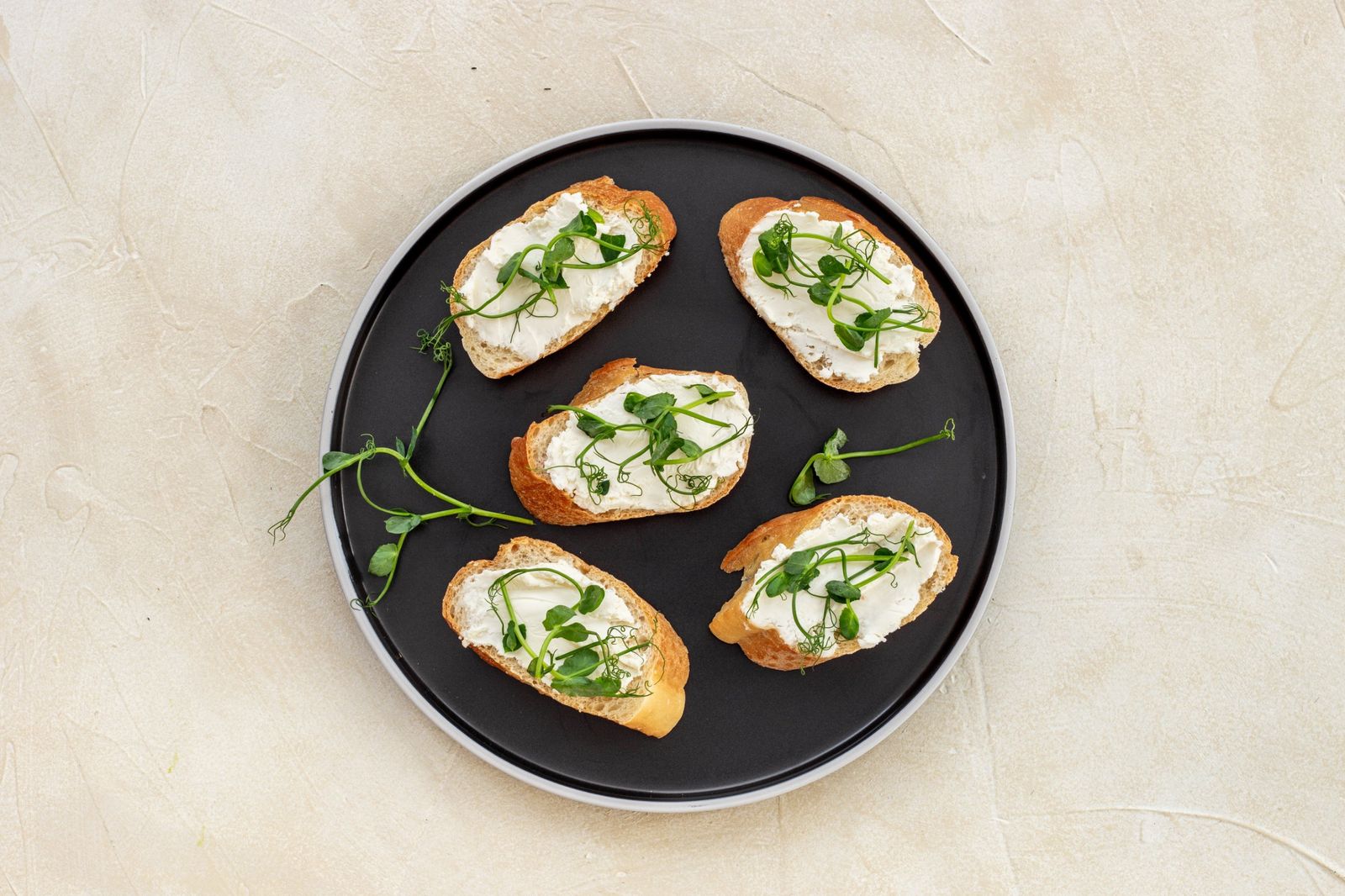 Crostini spread with soft cheese and topped with pea shoot microgreens