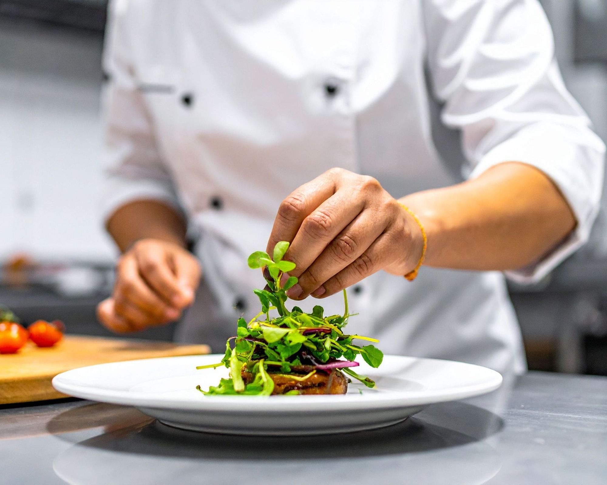 A chef placing fresh microgreens on a plated dish in a restaurant kitchen